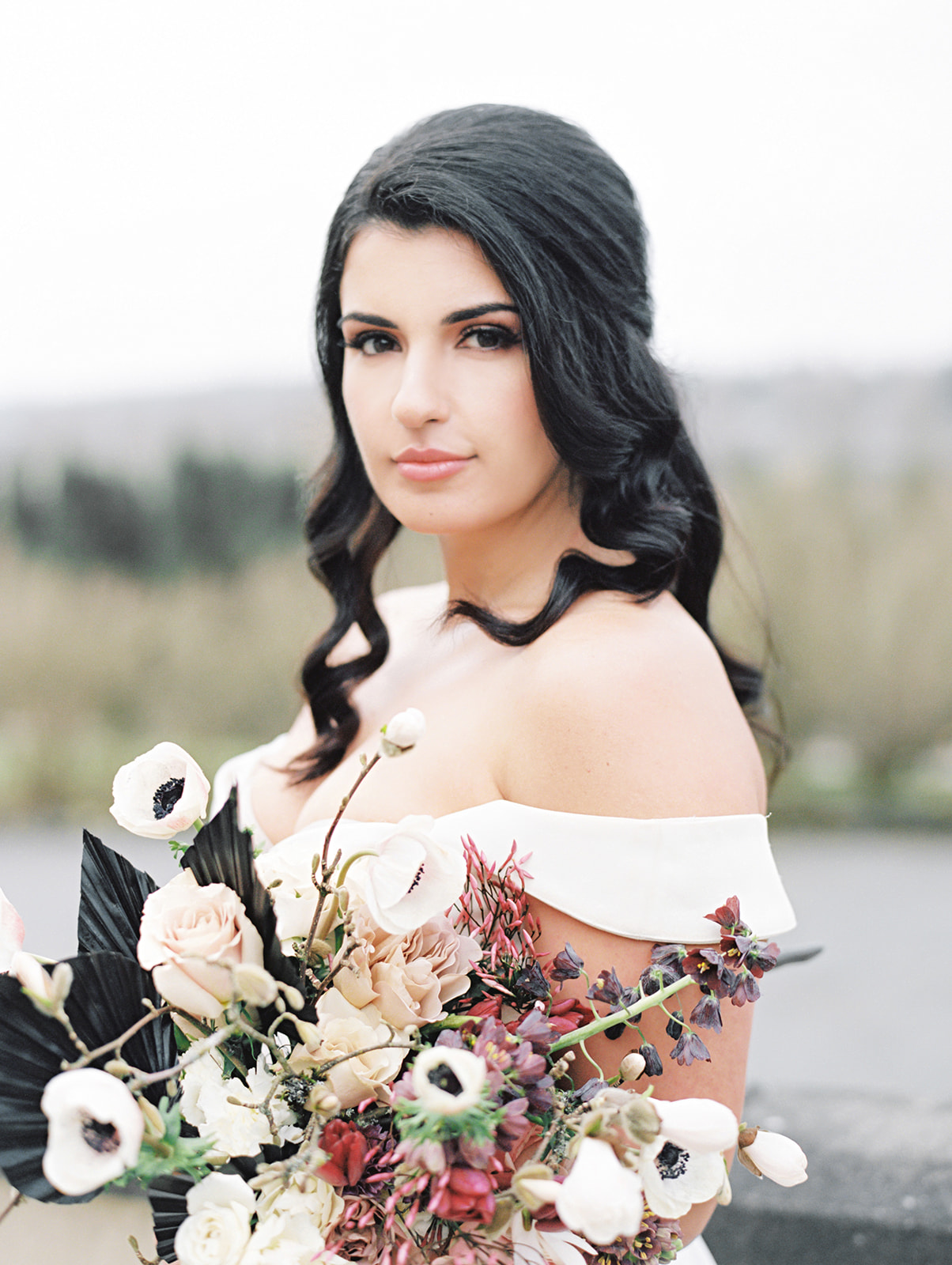 A bride holding a bouquet with anenomes, spring tulips and fritillaria, blooming branches, roses, and black palm spears