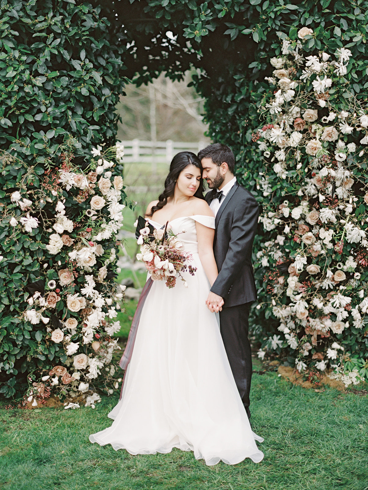 A bride and groom embracing in front of a floral arch installation in the garden hedge at Chateau Lill