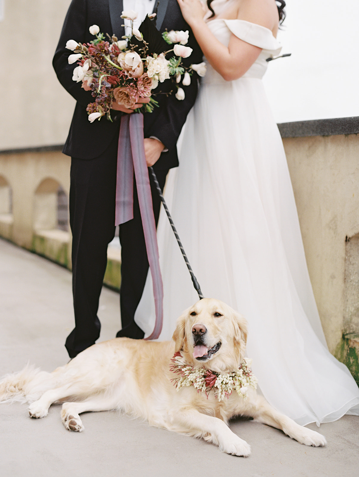 The couple standing and holding bouquet on the balcony of Chateau Lill, with Belle the dog laying in front
