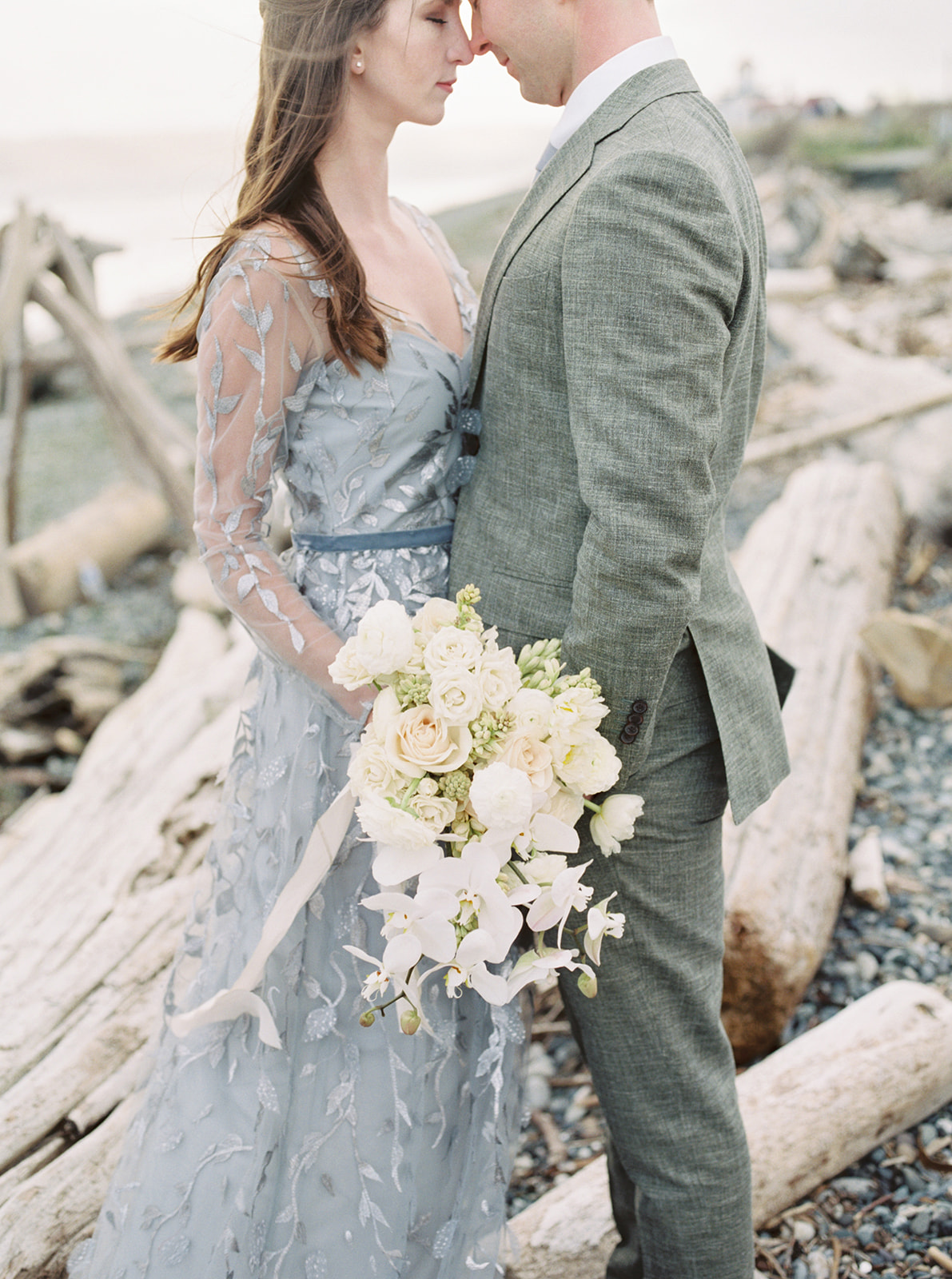 Couple standing in front of driftwood, holding bouquet
