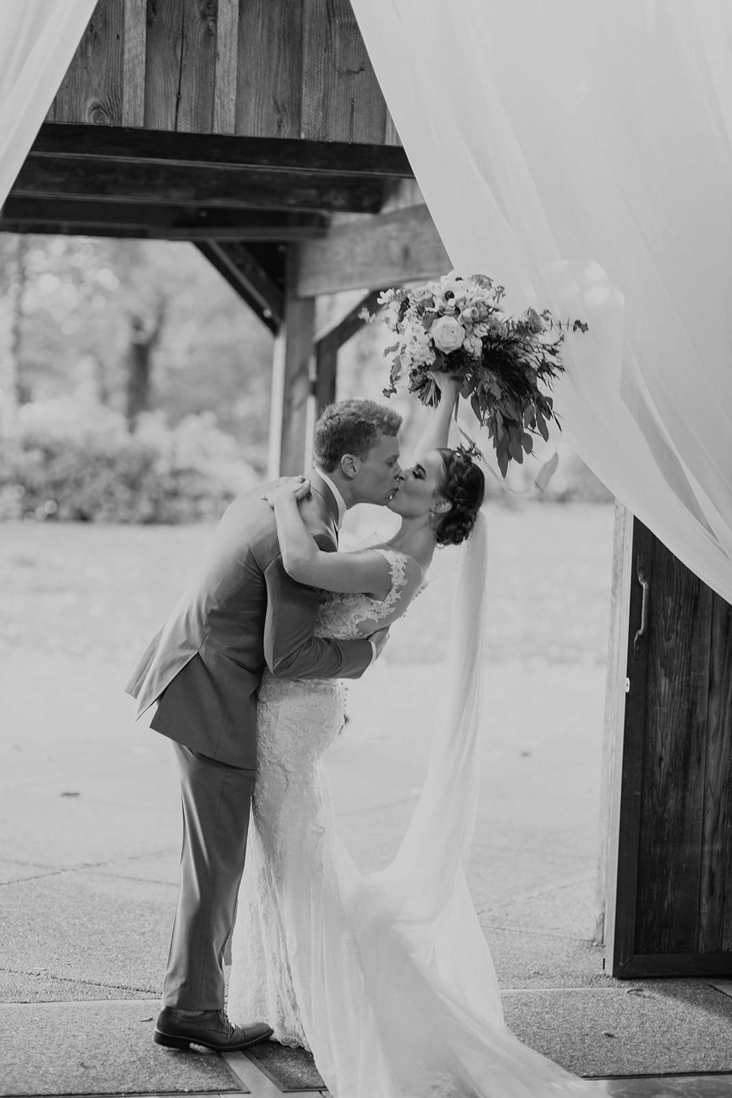 A black and white image of the bouquet being held high while couple kisses