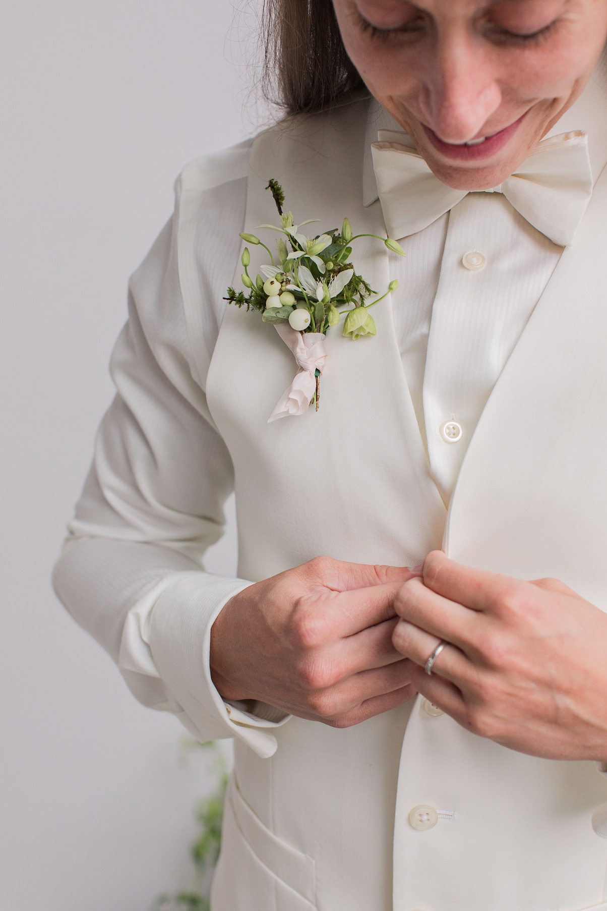 A bride with a boutonniere buttoning up a white vest
