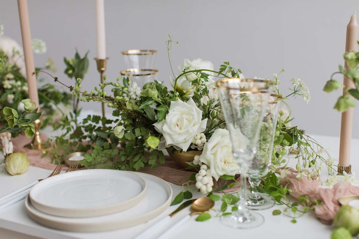 Table settings with stoneware plates, white floral arrangements, and tan taper candles