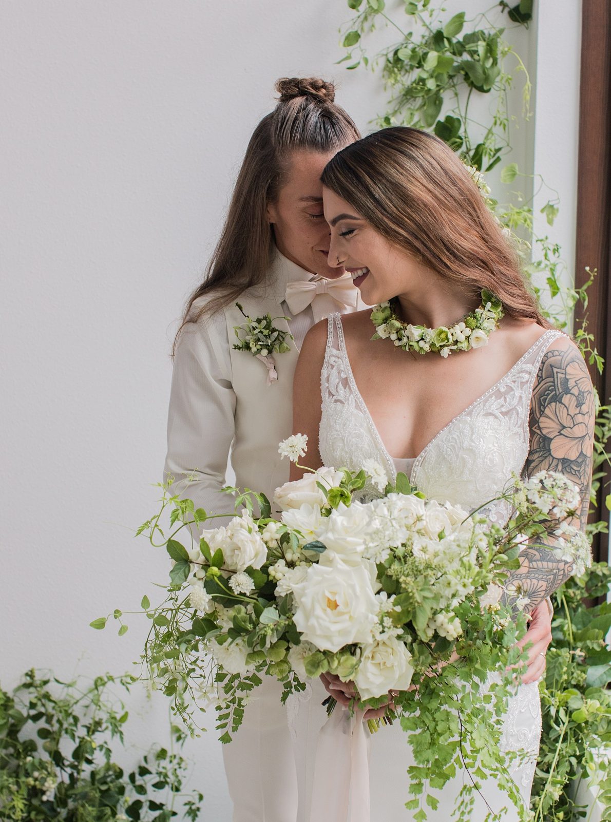 Two brides embracing, holding a white and green bouquet