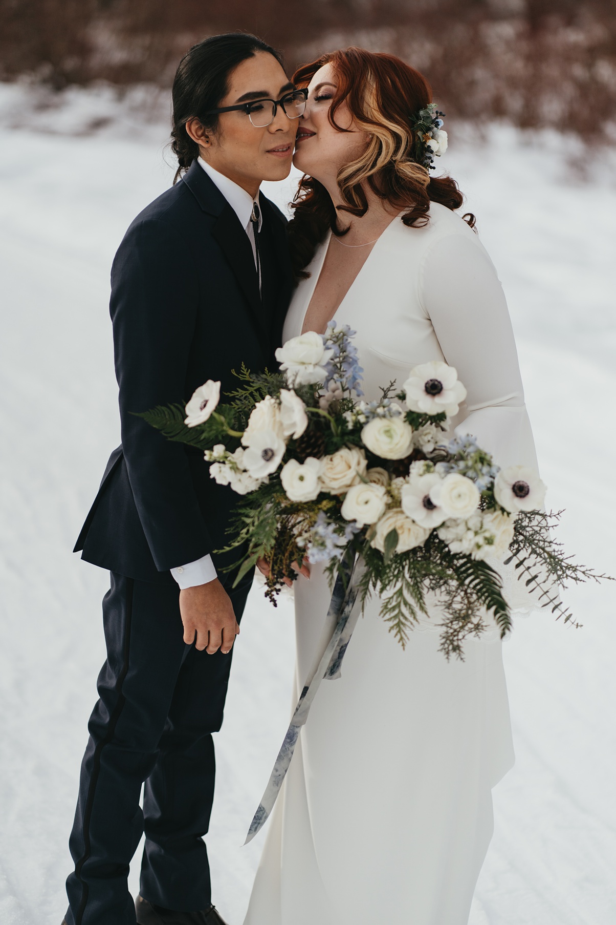 The couple embracing in the snow, holding the bouquet