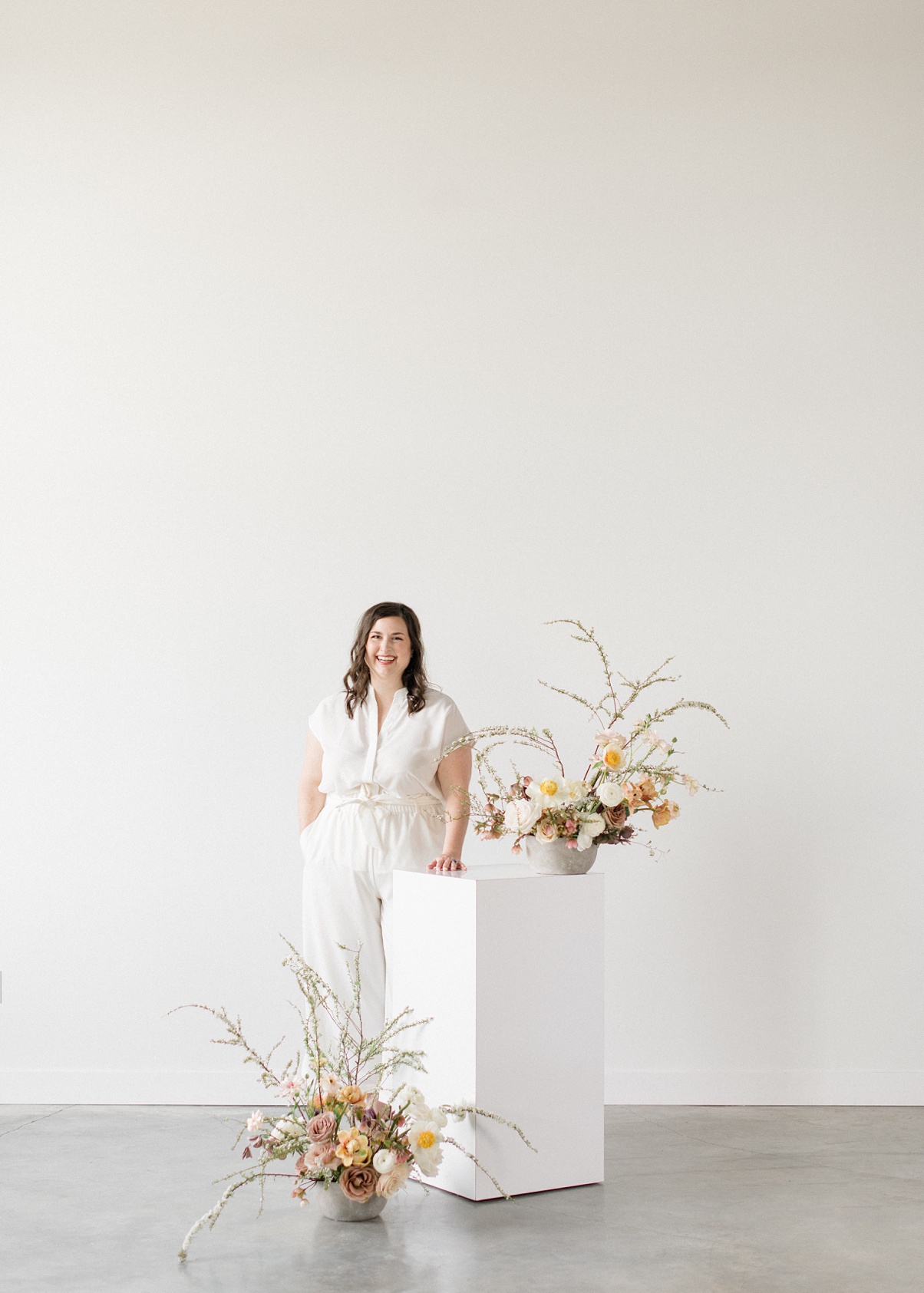 Owner Carolyn Kulb standing next to floral arrangements on a pillar