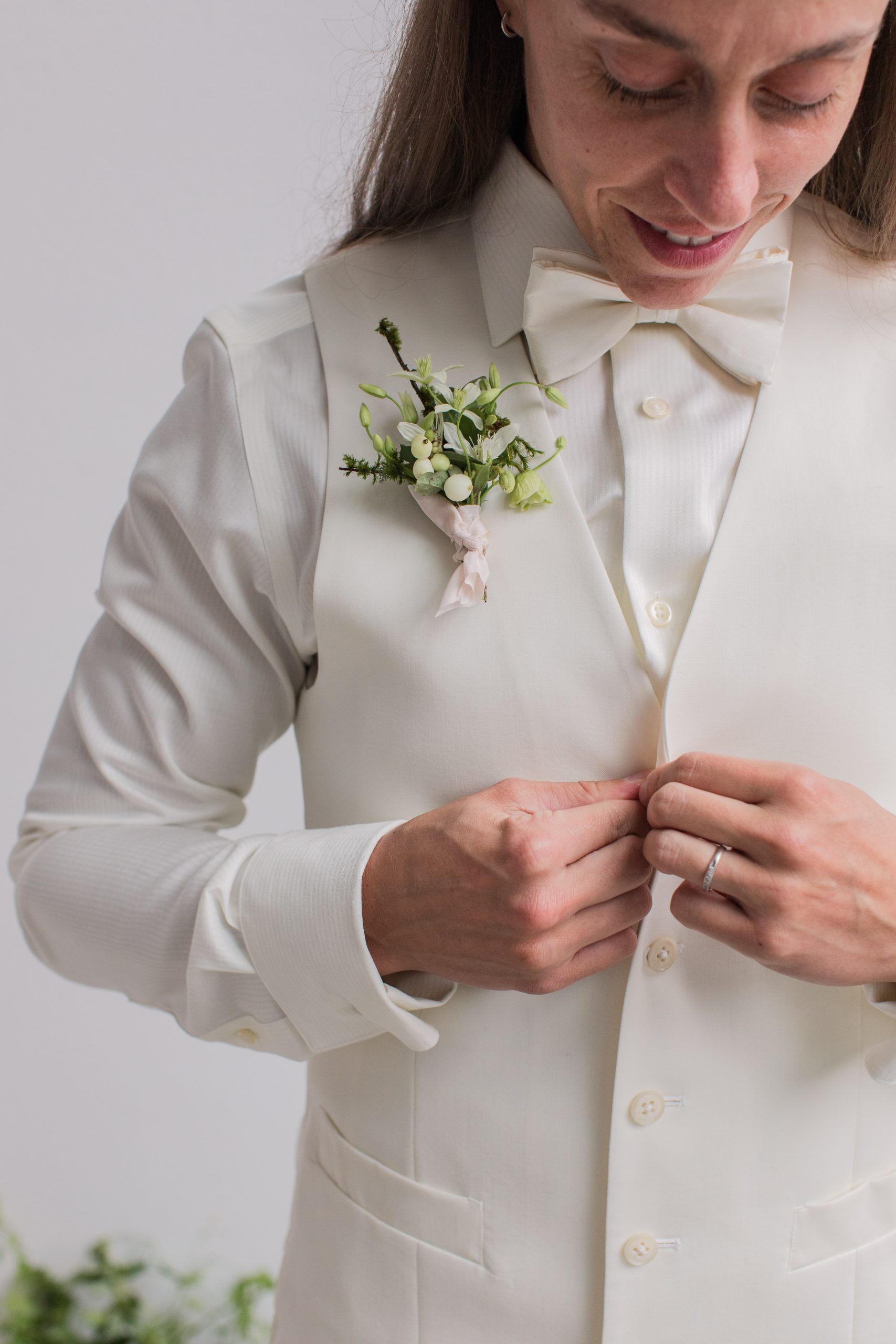 A queer bride buttons her vest before the wedding ceremony