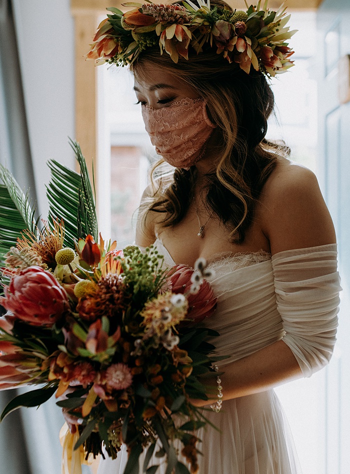 A bride in a mask holds her tropical wedding flower bouquet