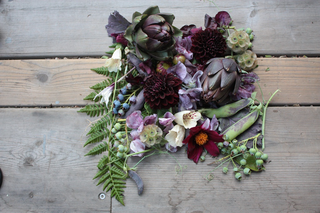 A flat lay of fun textures in July including berries, fern, artichokes, and more.