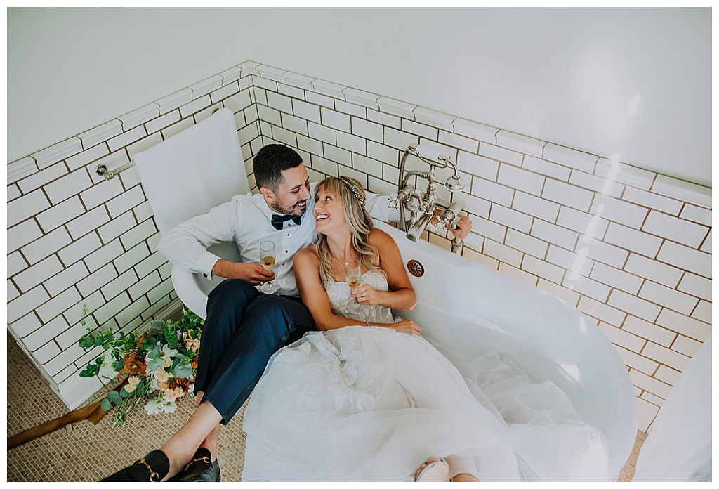 The couple sits in a bathtub with champagne