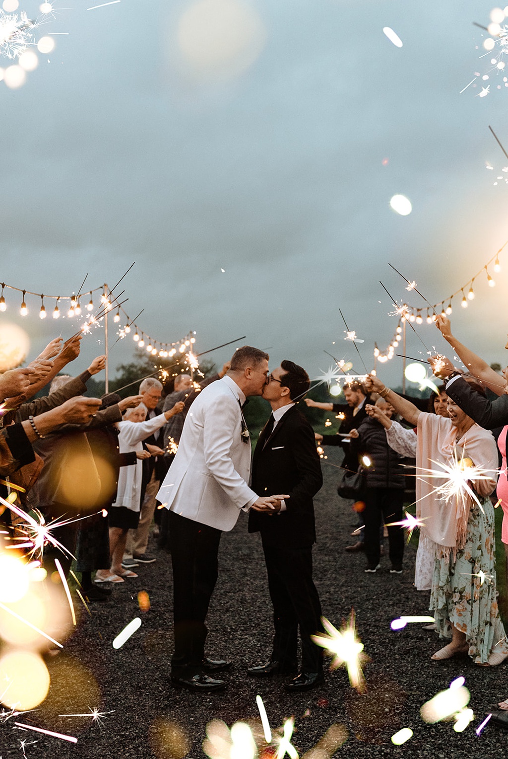 A sparkler exit at a gay wedding under cloudy skies
