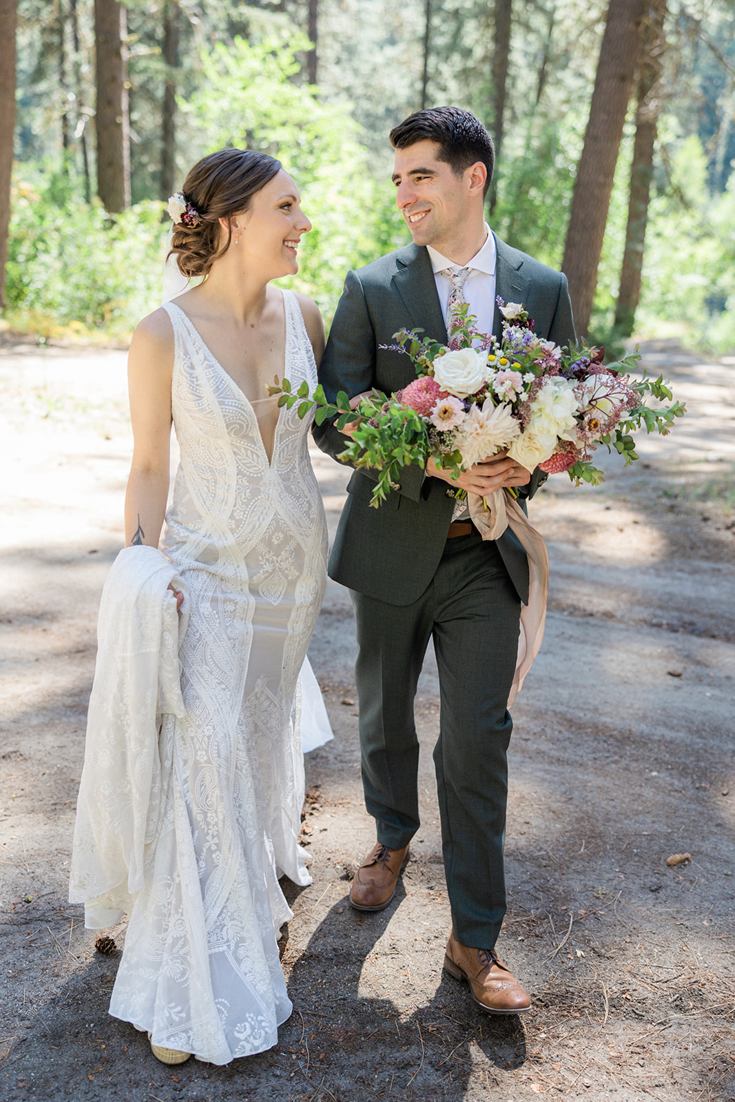 The bride and groom walk through the forest together, holding a bridal bouquet
