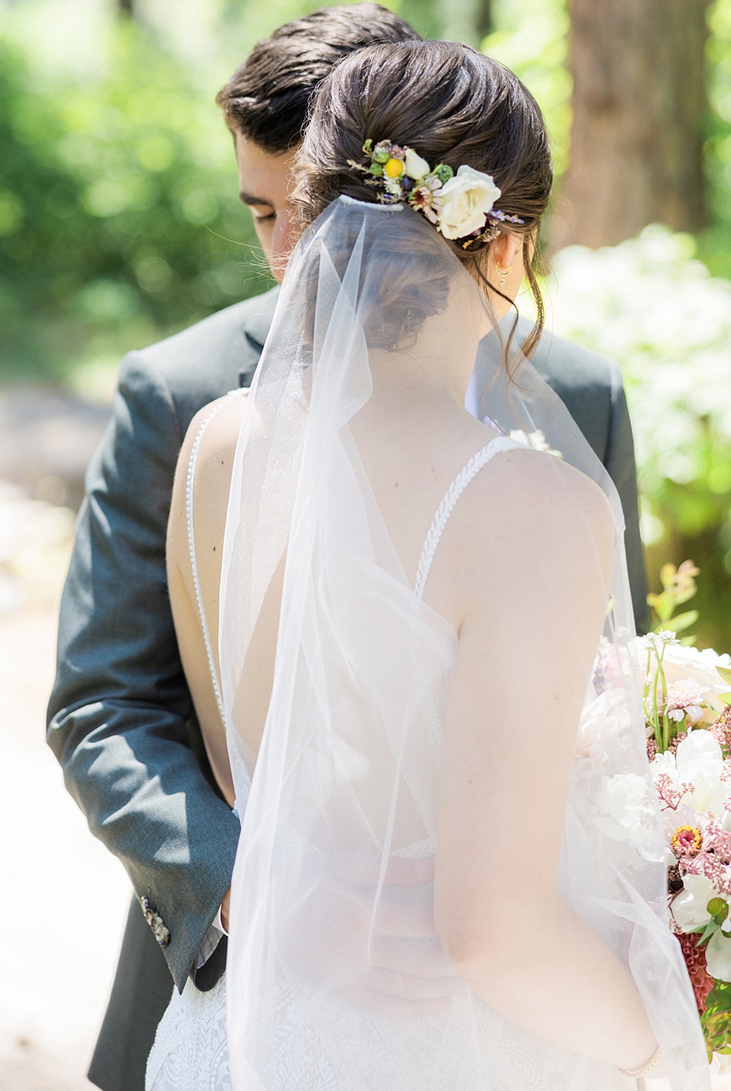 The bride and groom embrace, showing off her veil and hair flowers