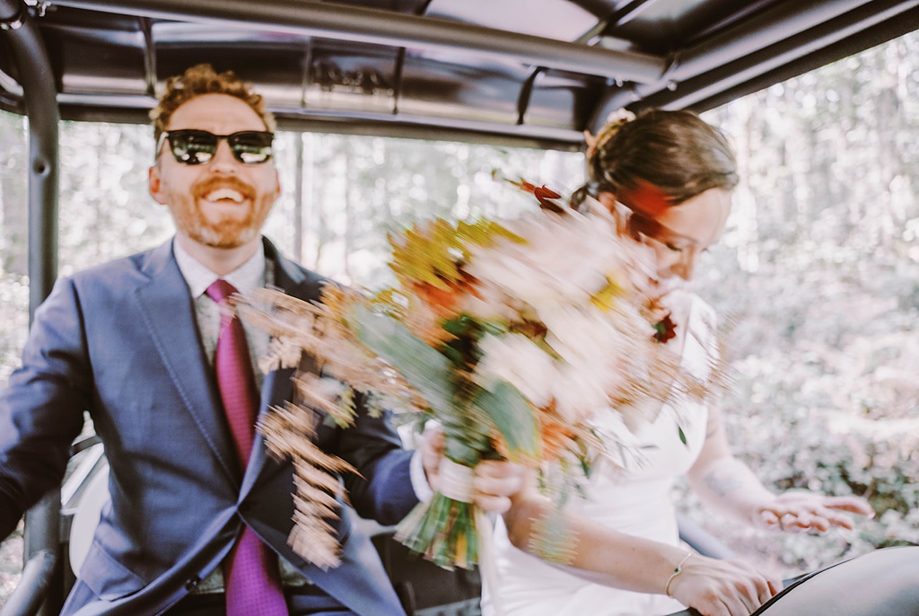 The groom holds the bouquet while the couple rides on a 4x4