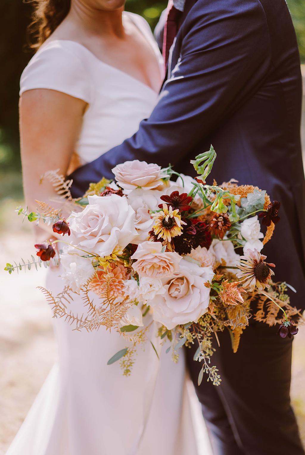 The couple holds a wedding bouquet for their late summer wedding