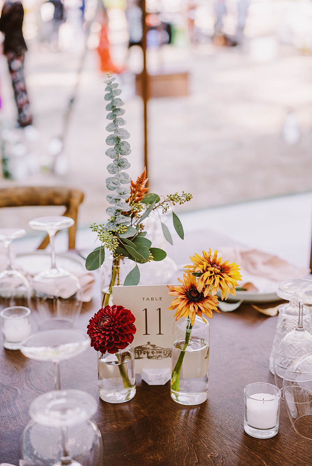 A table is set with bud vases, glassware, and candles for this summer wedding