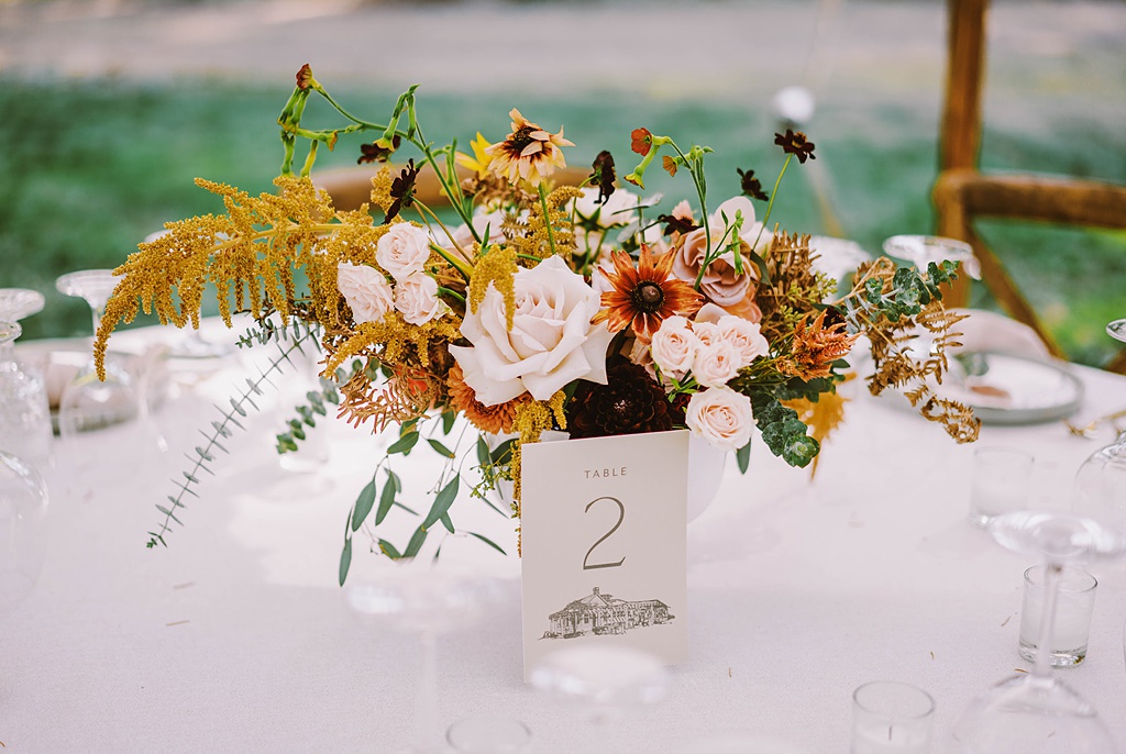 A gorgeous late summer wedding floral centerpiece sits on a white round table