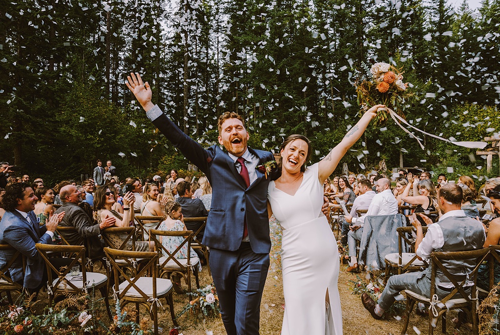 The couple walking down the aisle with "just married" smiles with confetti at their summer wedding
