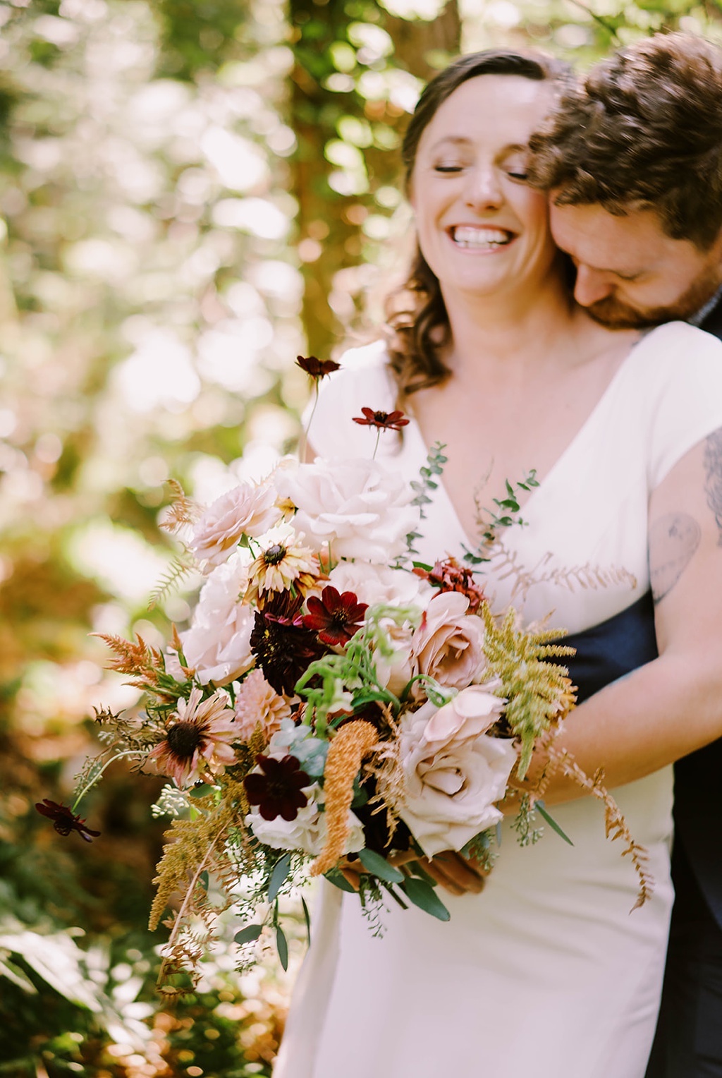 A couple laughing and holding a bouquet in this summer wedding