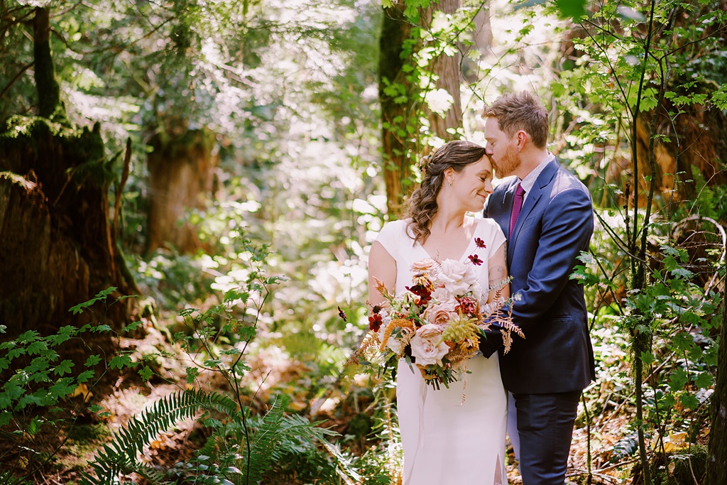 The couple standing in the forest holding the bouquet