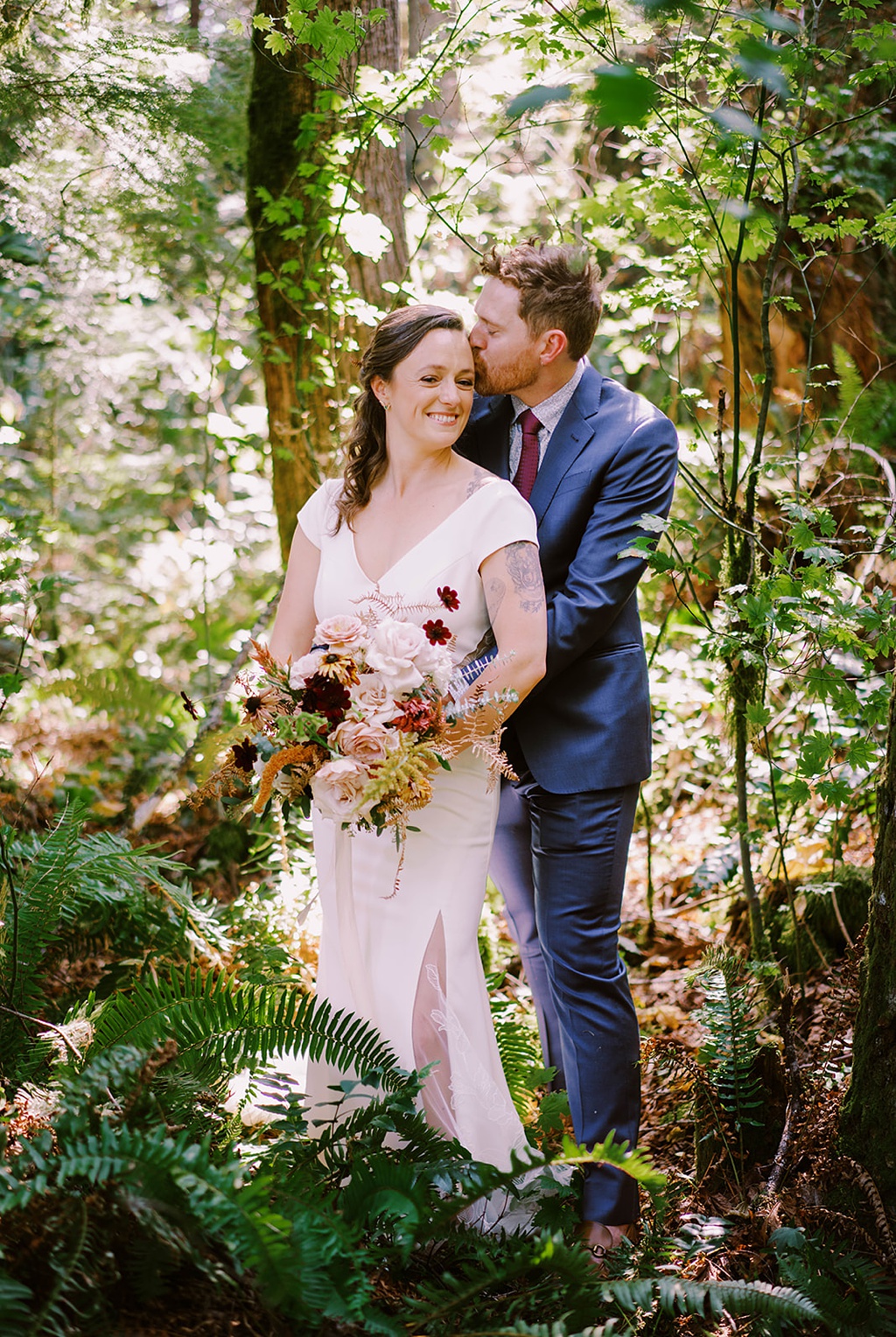 The couple stands in the forest holding the bridal bouquet