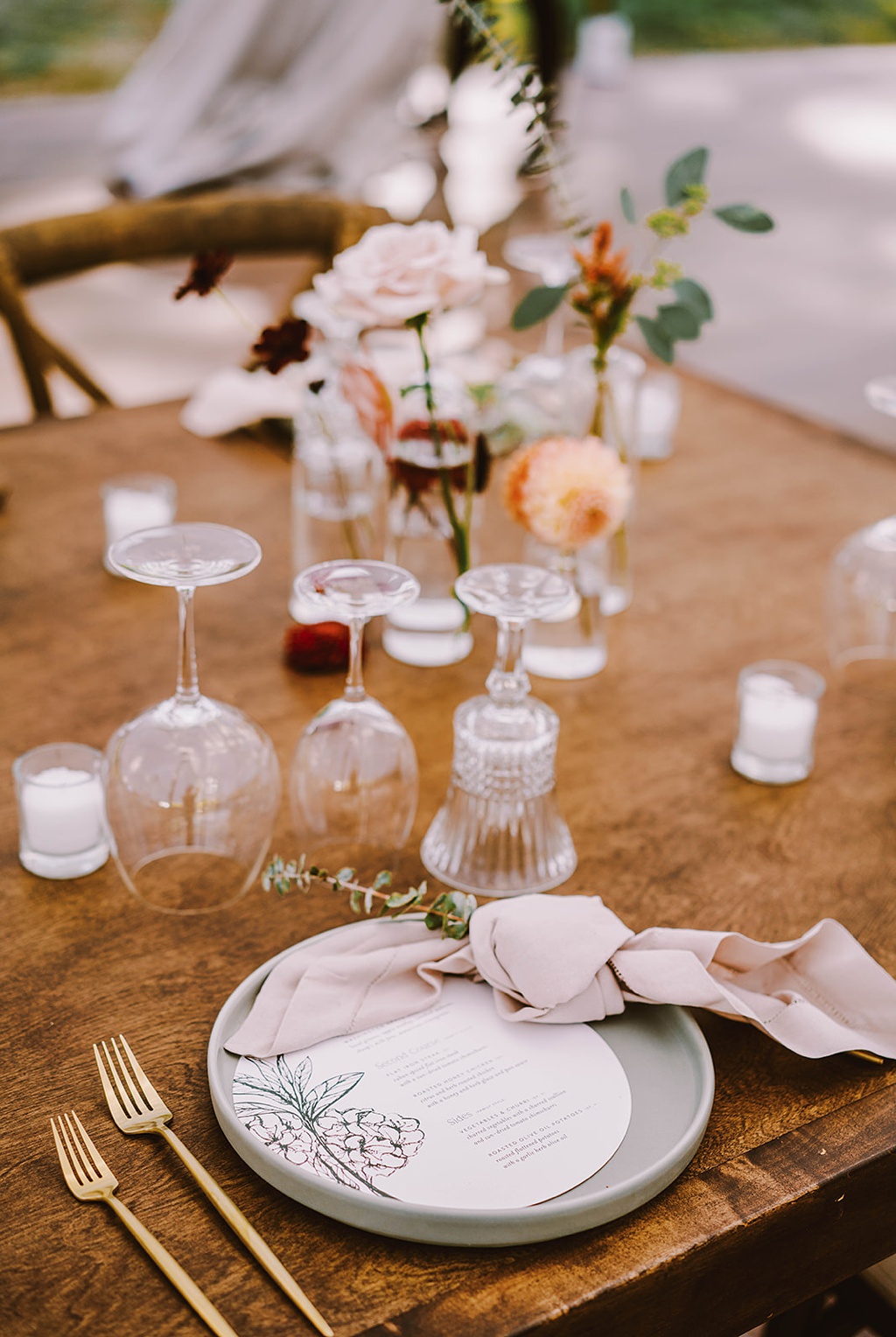 Reception place settings for a summer wedding with pink napkins, menus, and botanical sprigs