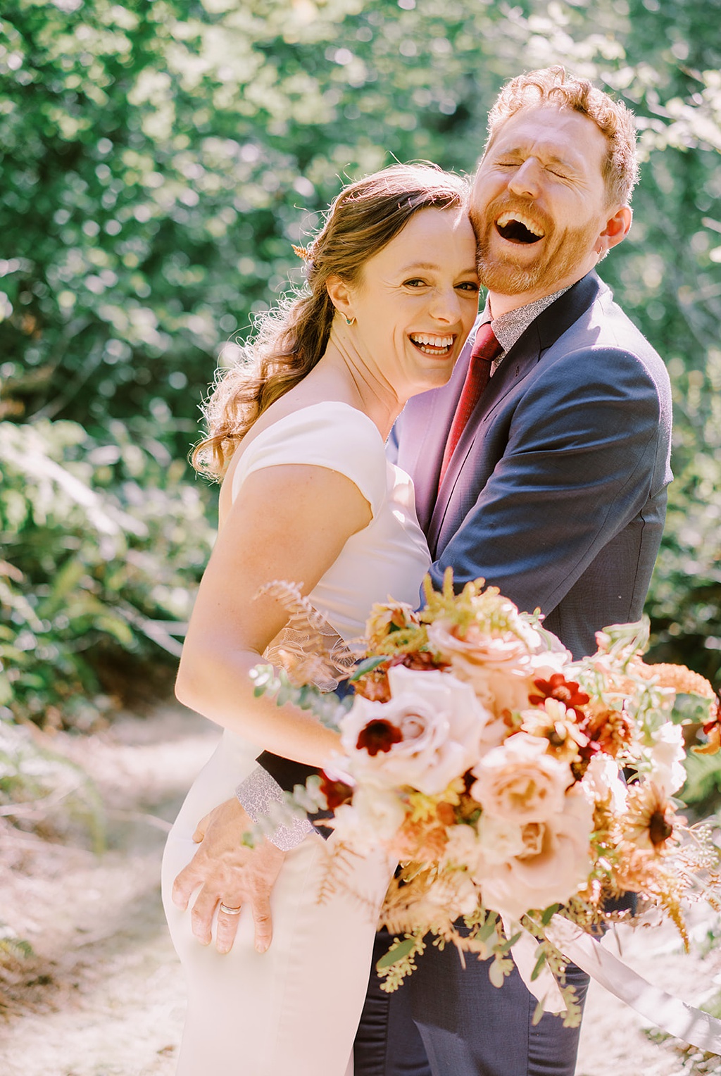 The couple laughing and holding a summer wedding flower bouquet